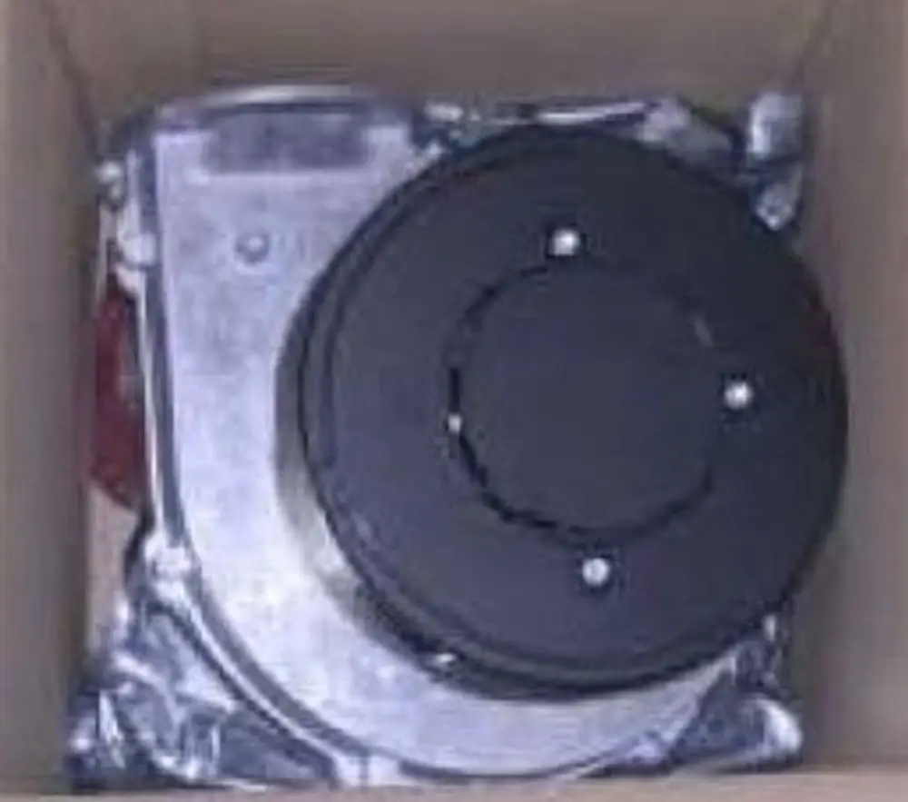 Brenner Gebläse von Remeha, in einem Karton verpackt. Die Konstruktion zeigt Metallteile und einen runden, schwarzen Abschnitt oben.